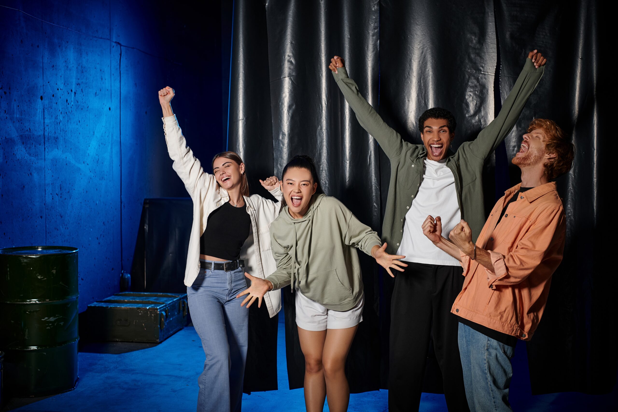 Four young people celebrate excitedly in a vibrant, blue-lit space, showcasing energy and joy. Their expressions convey enthusiasm and camaraderie.
